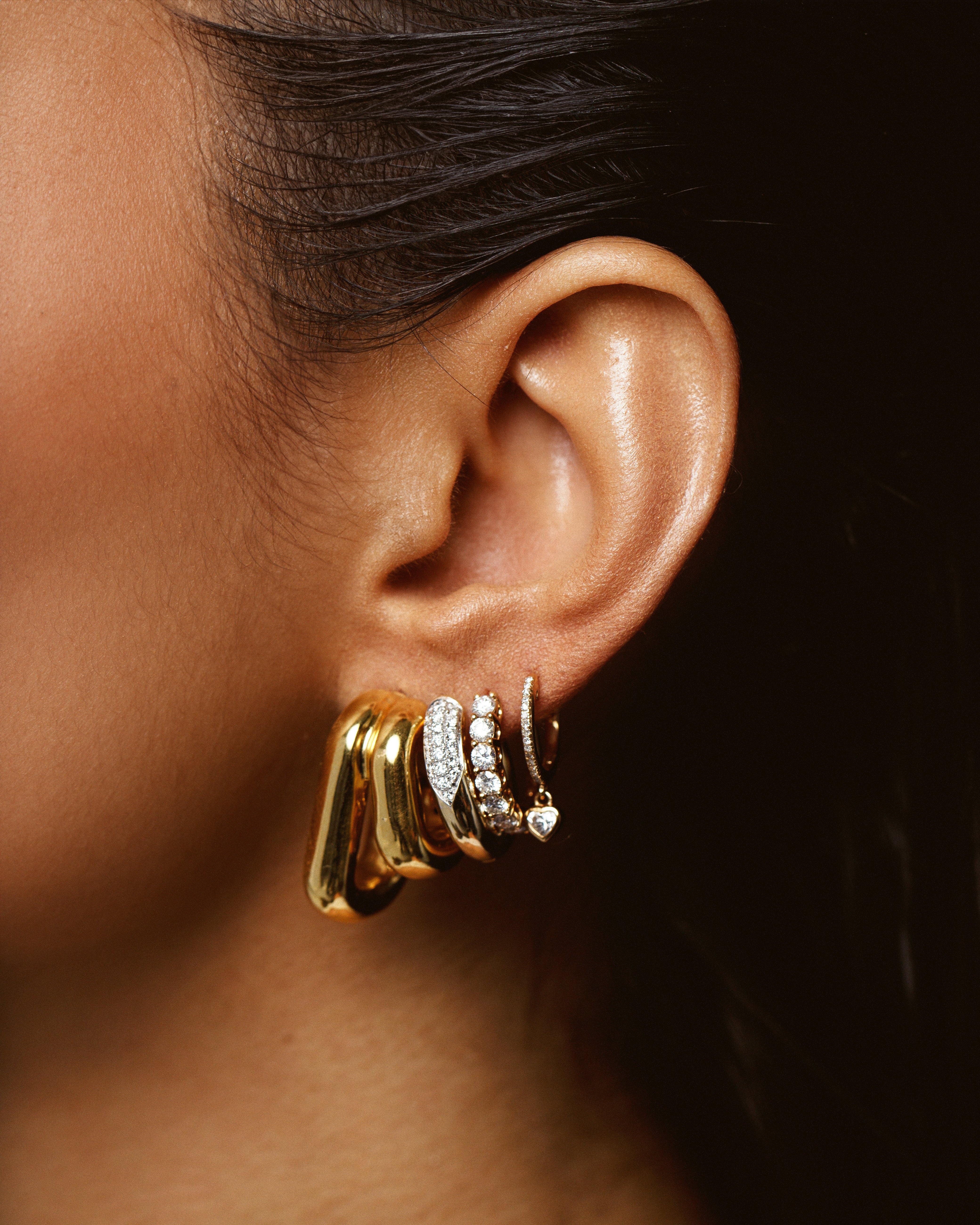 multiple gold huggies and gold and diamond hoop earrings shown on model's ear